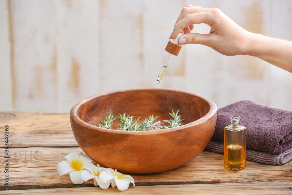 Woman pouring essential oil from bottle into bowl at home