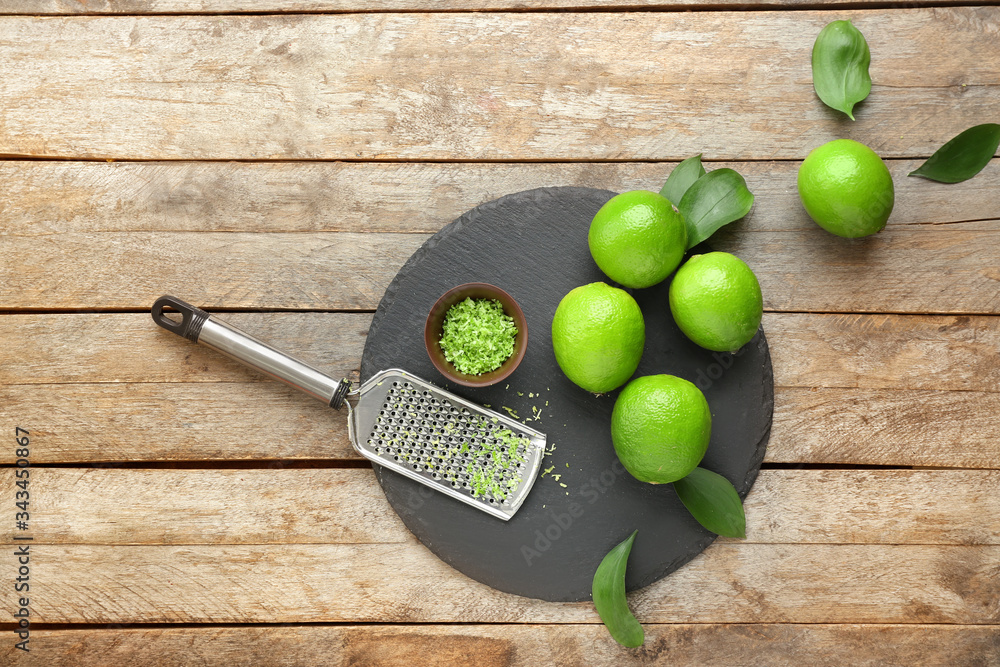 Fresh limes with grater on wooden background