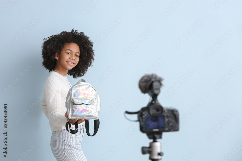 African-American teenage fashion blogger recording video on color background