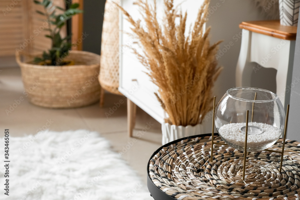 Glass holder with candle and wicker mat on table in room