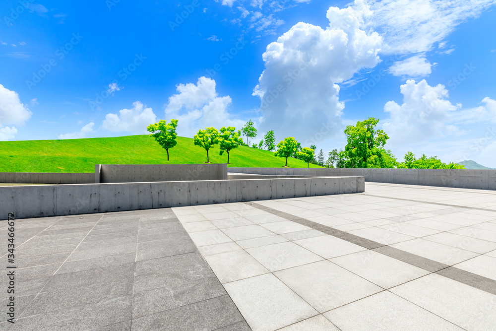 Empty square ground and green grass with tree under blue sky.