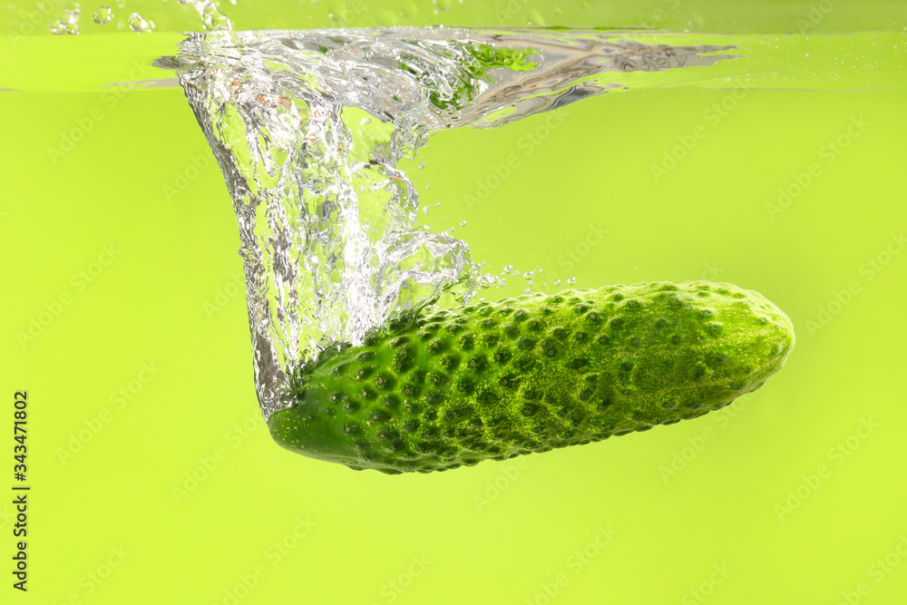 Falling of fresh cucumber into water against color background