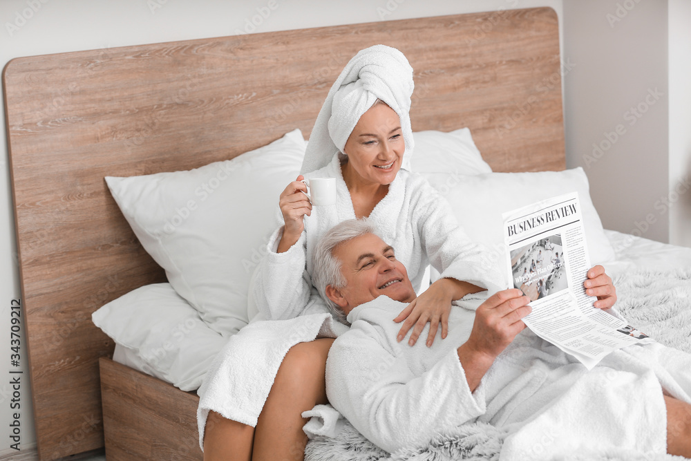 Mature couple reading newspaper in bedroom