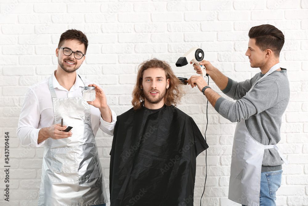 Young hairdressers working with client against white brick background