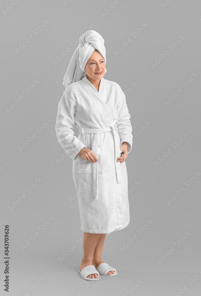 Mature woman in bathrobe on grey background