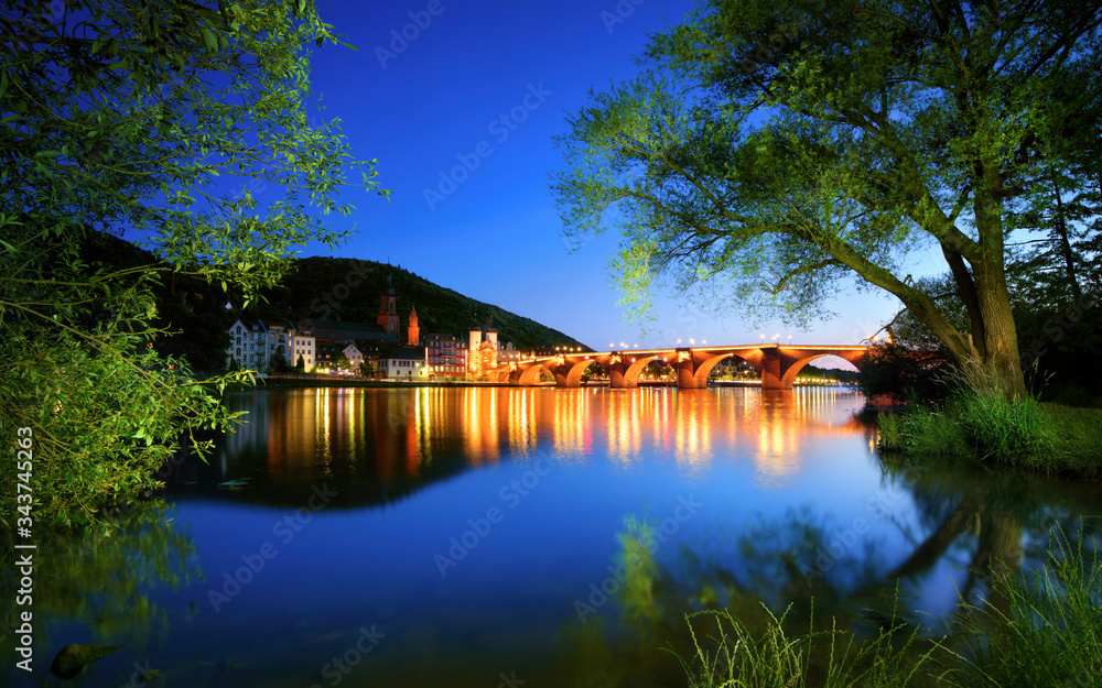 Neckar river in Heidelberg, Germany, at dusk, with deep blue sky reflected in the clear water and gr