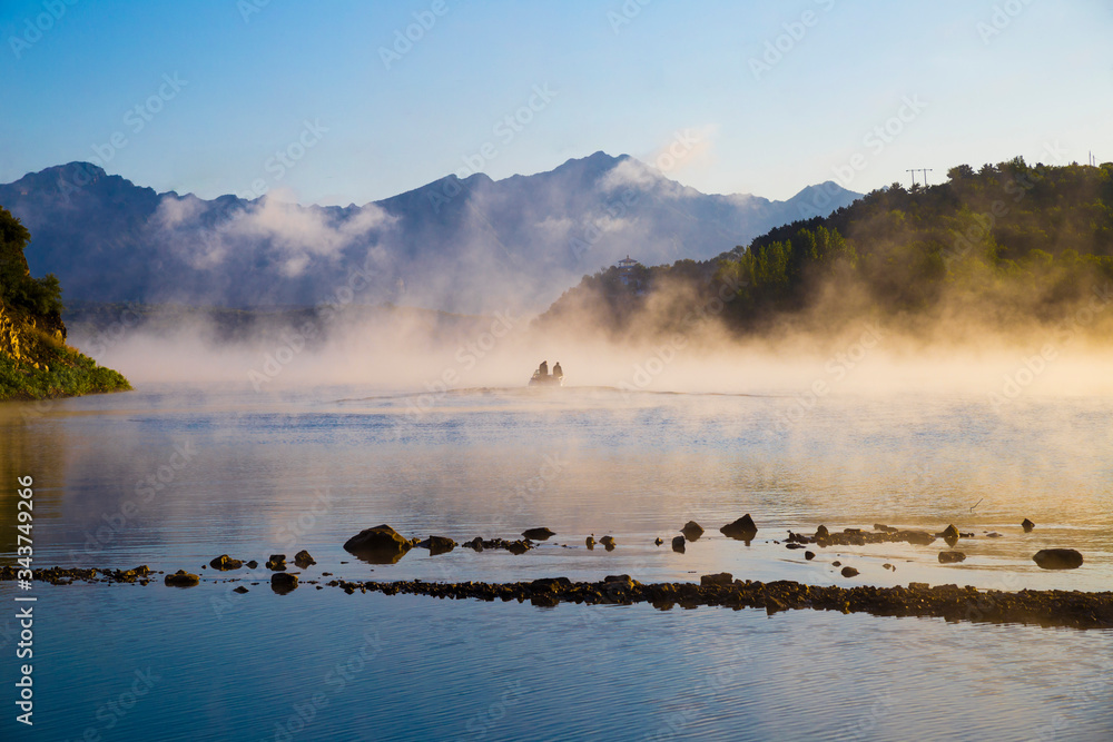 Concept mysterious landscape of a boat with two fisherman at misty lake