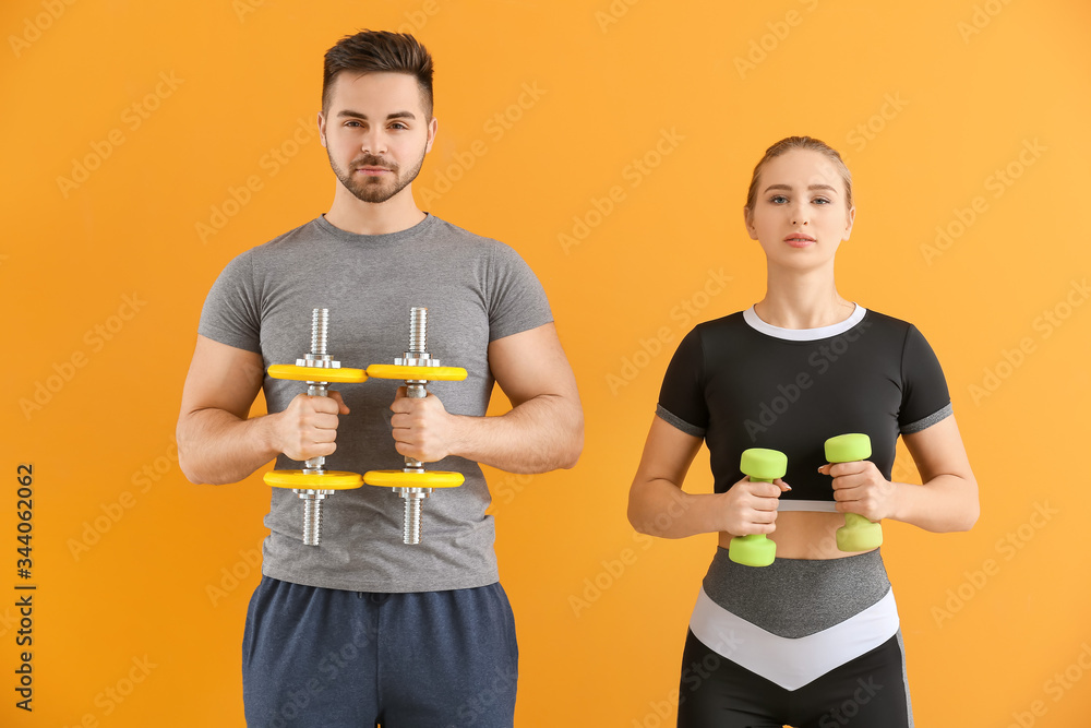 Sporty young couple training with dumbbells on color background