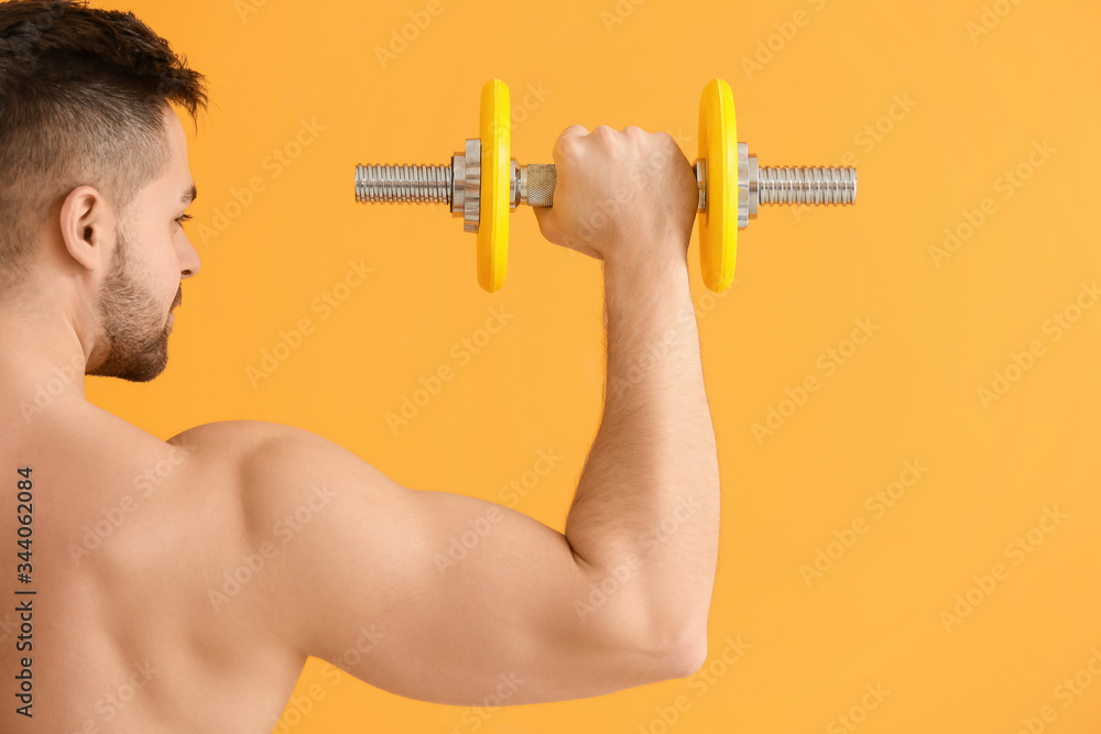 Sporty young man training with dumbbells on color background