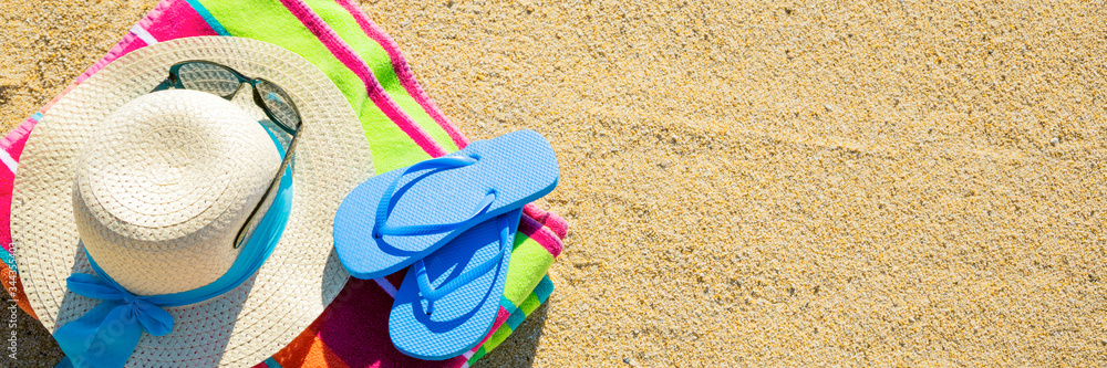 Beach towel with hat, sunglasses and flip flops photographed from above on sandy beach, hot summer d