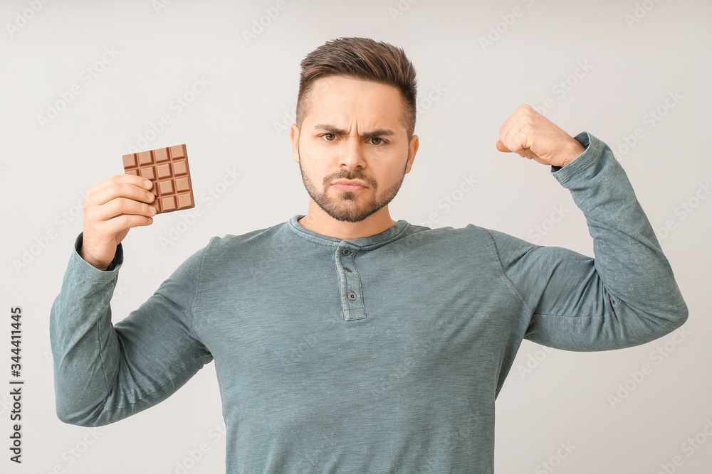 Strong young man with tasty chocolate on light background