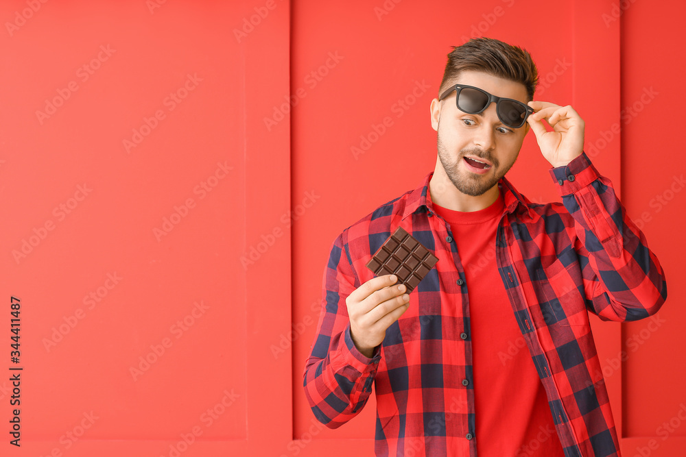 Surprised young man with tasty chocolate on color background