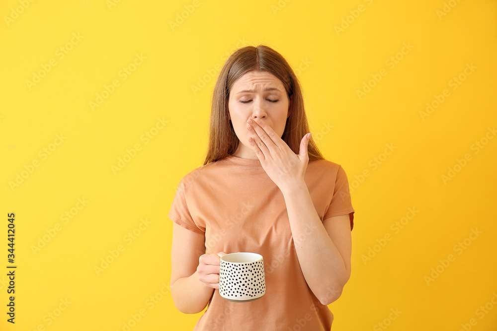 Sleepy young woman with coffee on color background