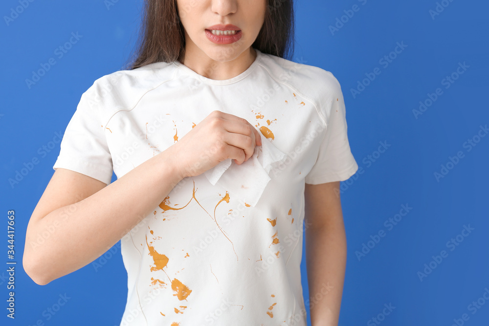 Young woman wiping dirt from clothes on color background