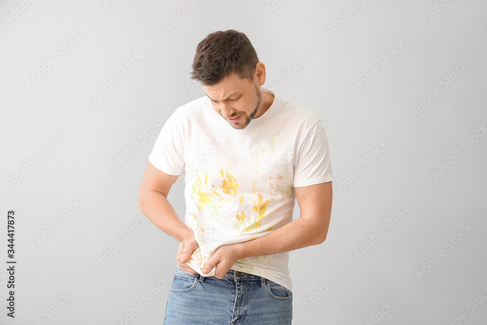 Displeased man in dirty clothes on light background