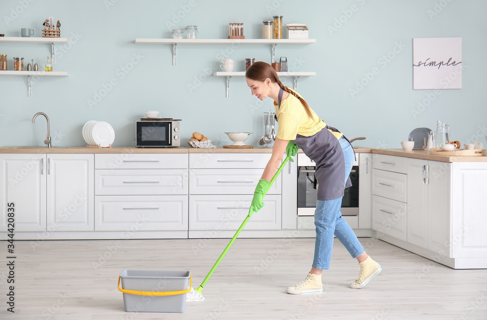 Young woman mopping floor in kitchen