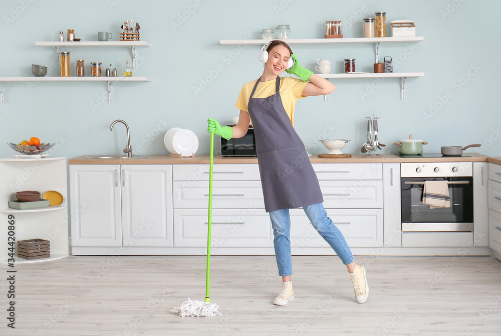 Young woman having fun while mopping floor in kitchen