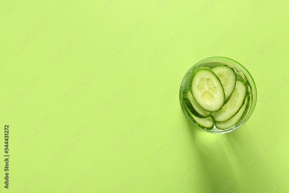 Glass of cucumber infused water on color background