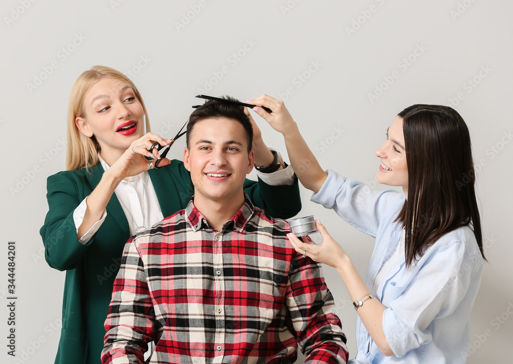 Young hairdressers working with client against light background