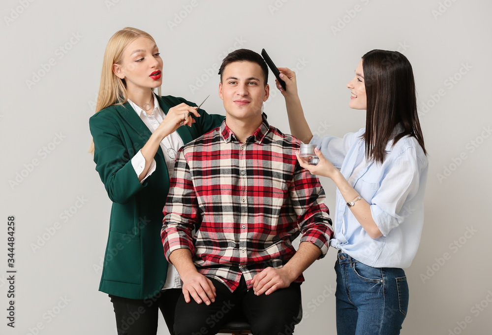 Young hairdressers working with client against light background