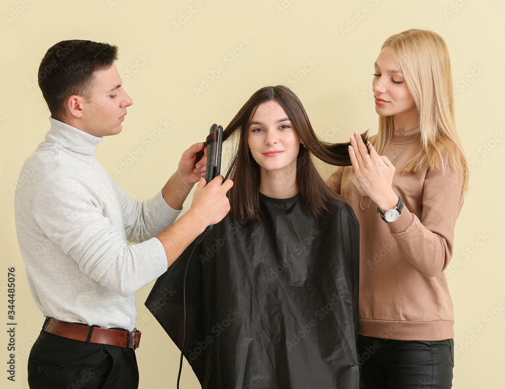 Young hairdressers working with client against color background