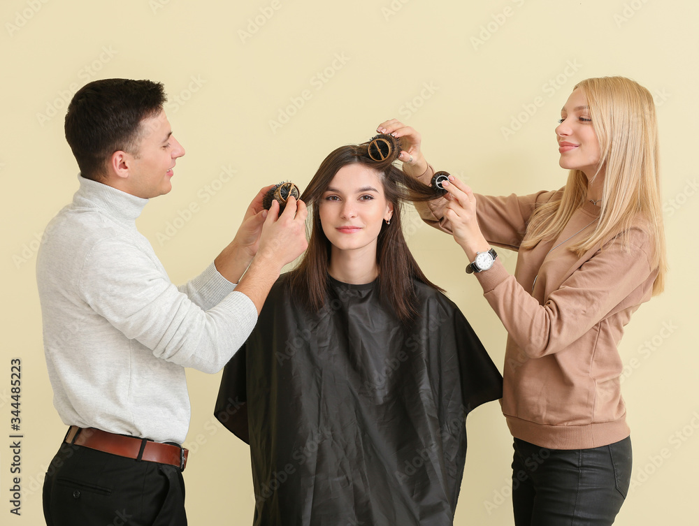 Young hairdressers working with client against color background