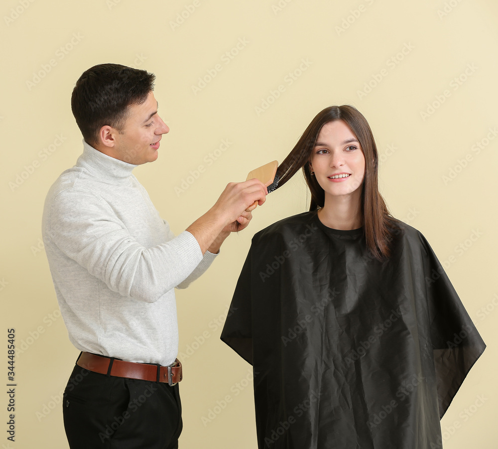 Young hairdresser working with client against color background