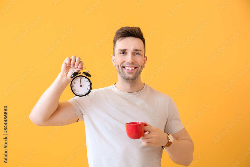 Young man with coffee and alarm clock on color background