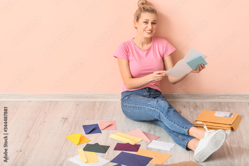 Young woman with many letters sitting near color wall