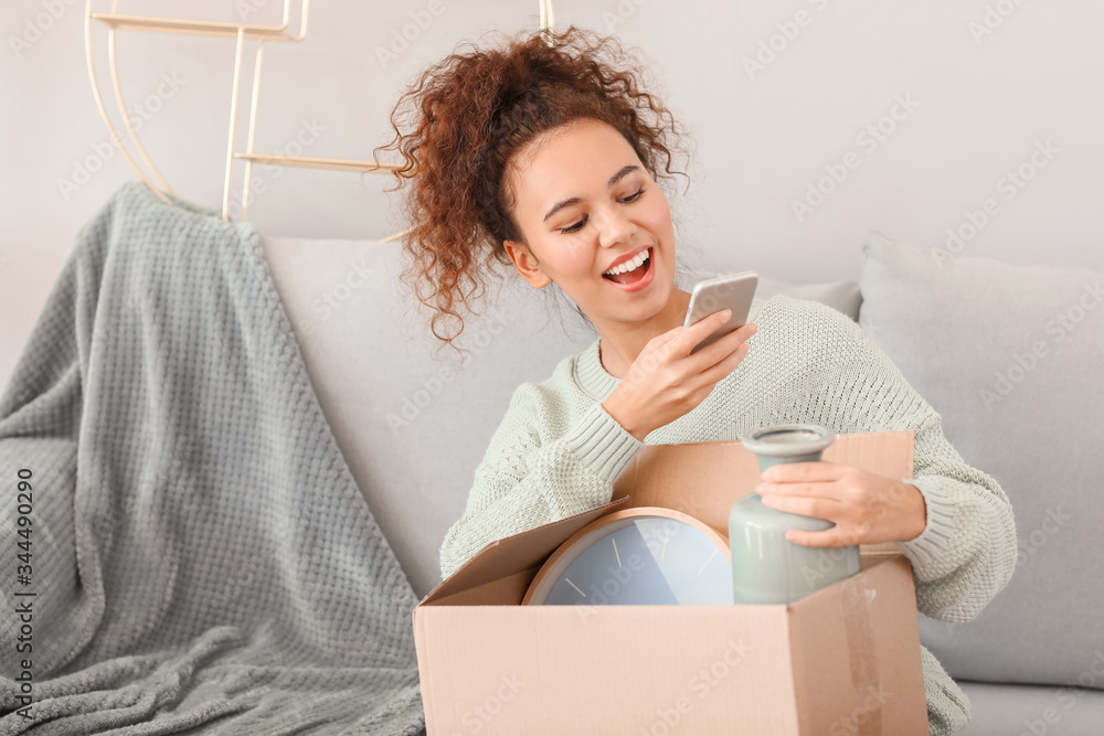 Young woman with moving box taking photo in her new home