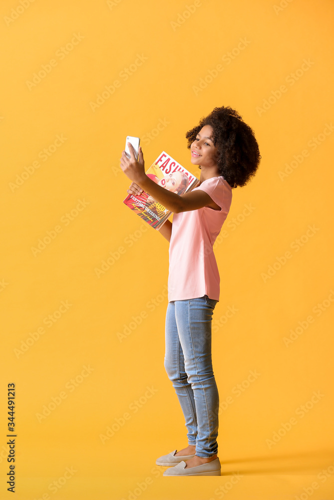 African-American teenage fashion blogger with mobile phone on color background