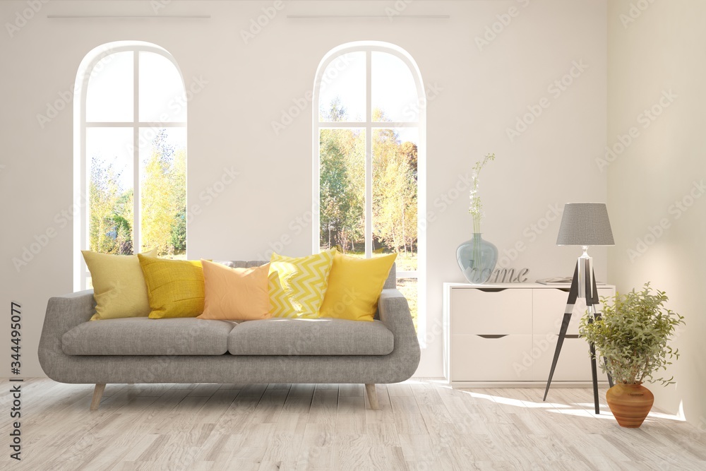 Stylish room in white color with sofa and autumn landscape in window. Scandinavian interior design. 