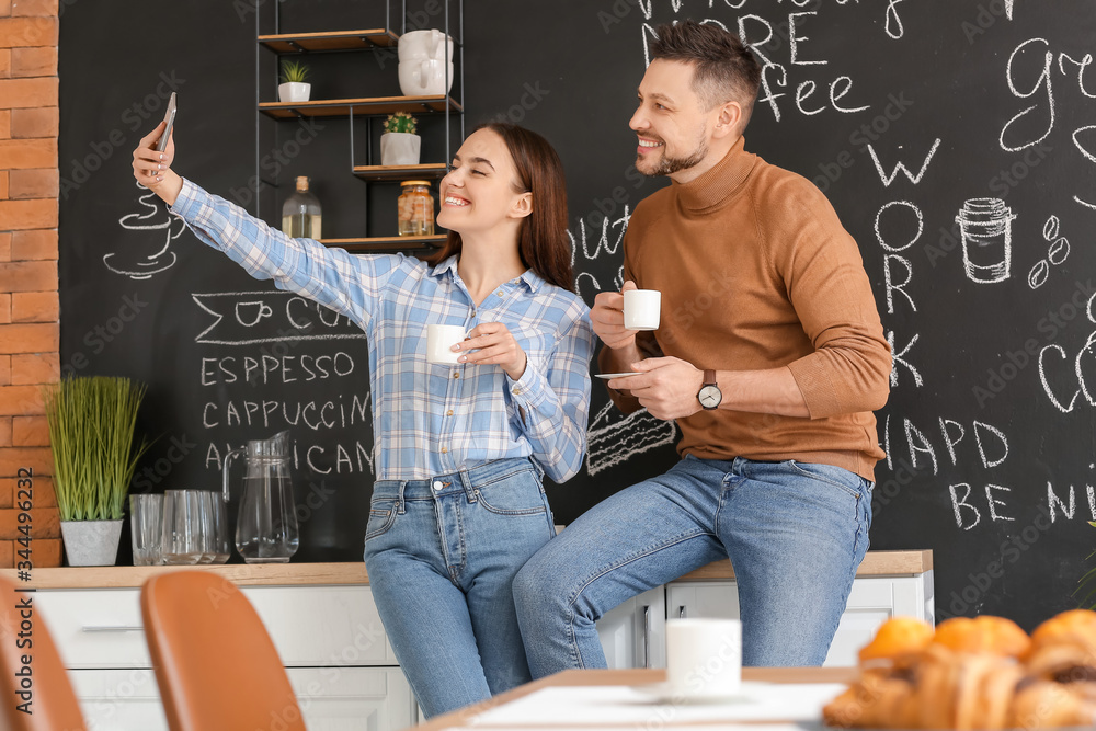 Colleagues taking selfie while drinking coffee in kitchen of office