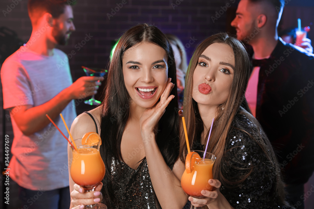 Happy young women with cocktails in night club