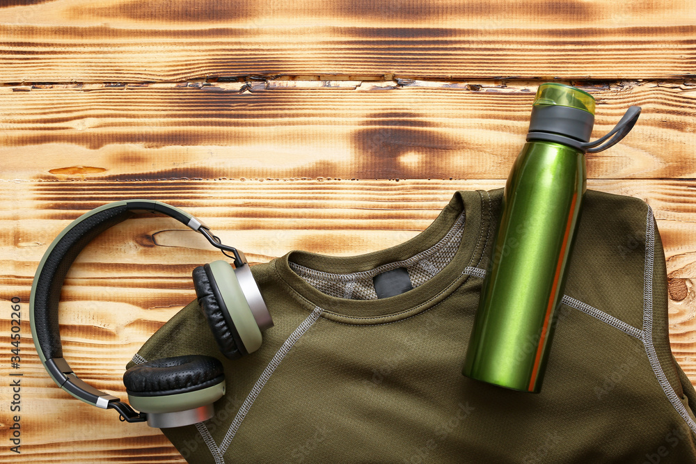 Sportswear, headphones and bottle of water on wooden background