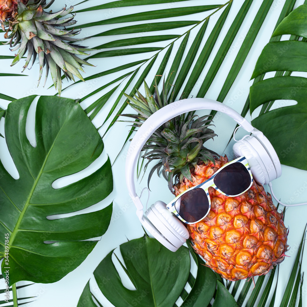 Funny pineapple wearing white headphone, concept of listening music, isolated on blue background wit