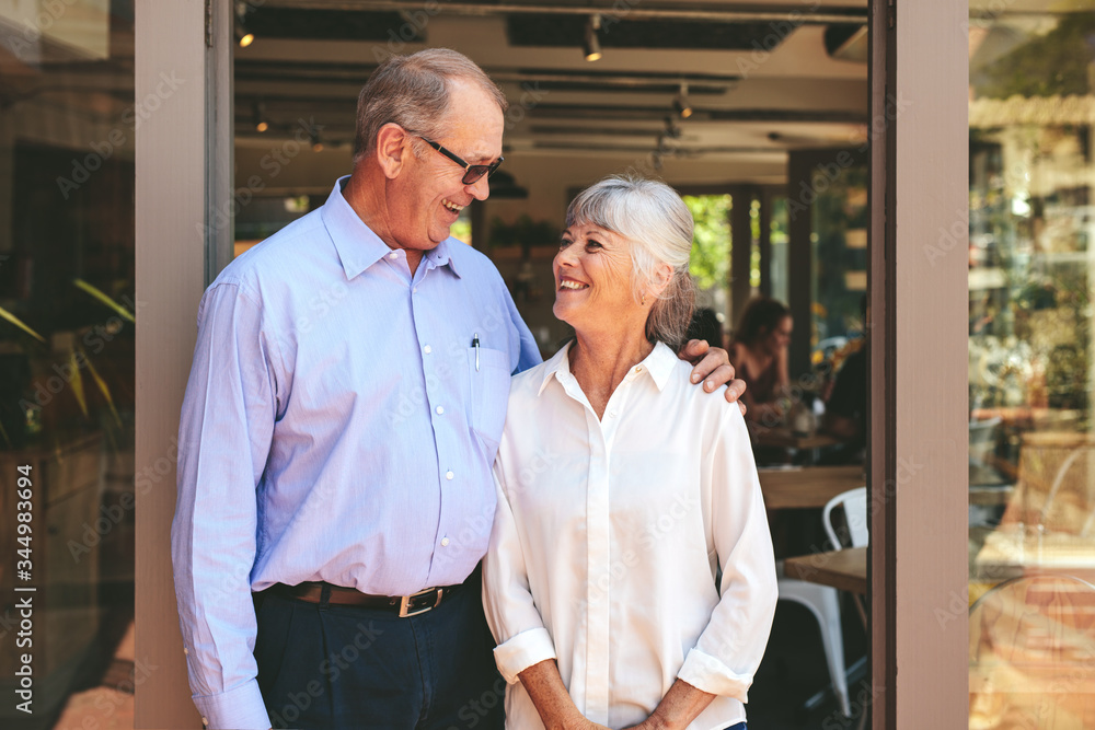 Senior couple standing at the entrance of their cafe