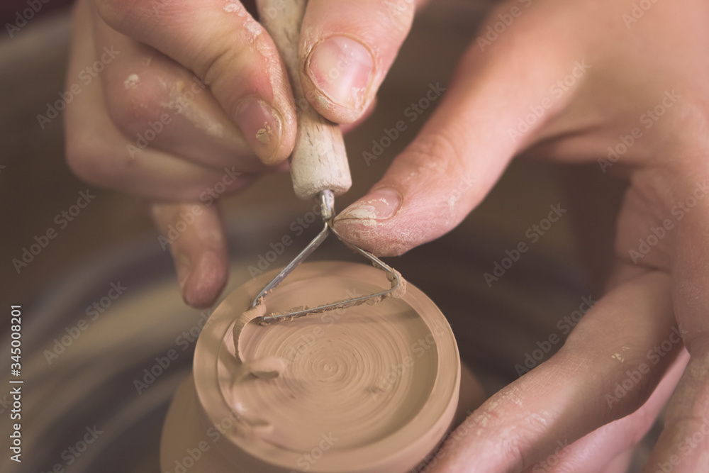 Master removes the top layer of clay on pot with a special tool.