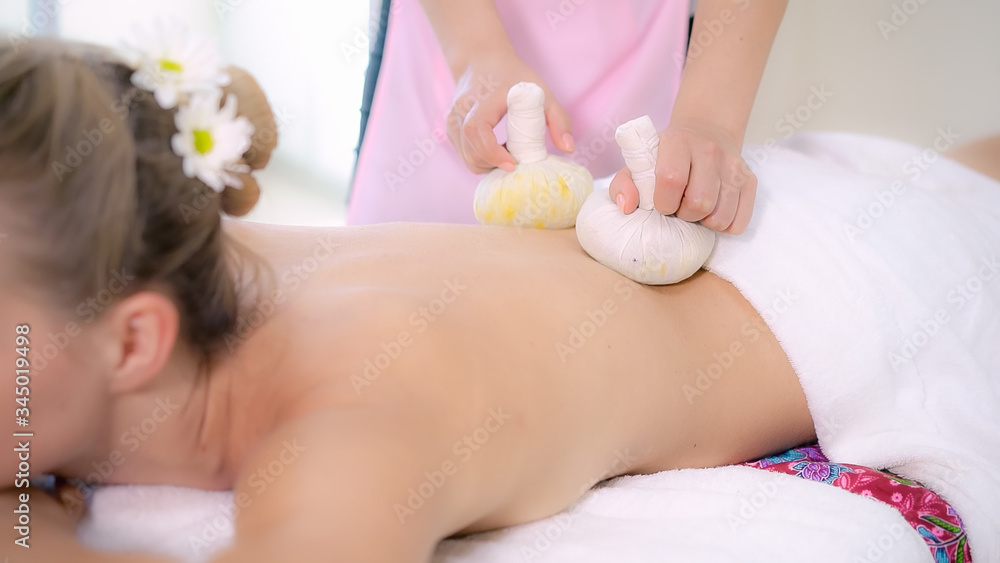 Massage therapist holds a herbal compress to do treatment to woman lying on spa bed in a luxury spa 