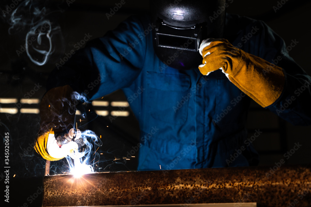 Metal welder working with arc welding machine to weld steel at factory while wearing safety equipmen