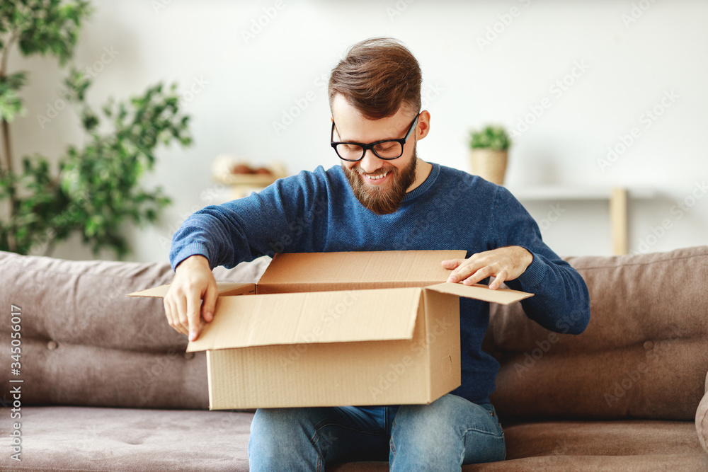 Happy man unpacking delivery box on sofa.