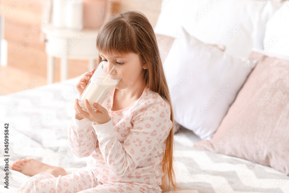 Little girl with glass of milk in bedroom