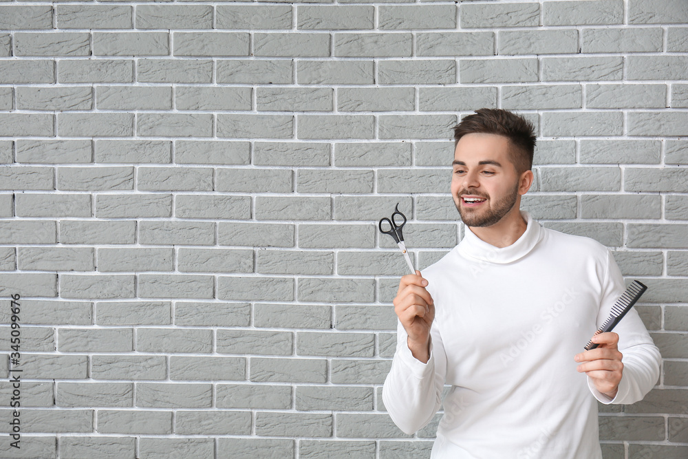 Handsome young man with comb and scissors on brick background