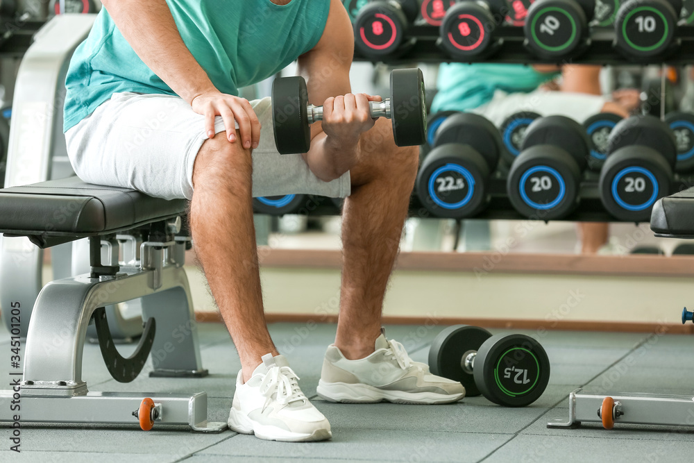 Sporty young man training with dumbbells in gym