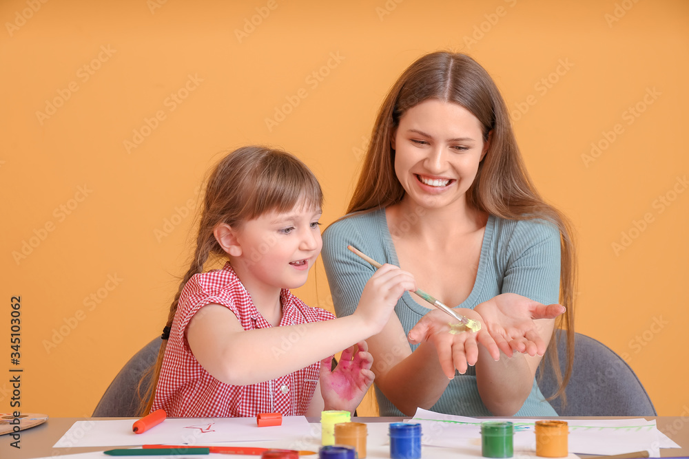 Drawing teacher giving private art lessons to little girl on color background