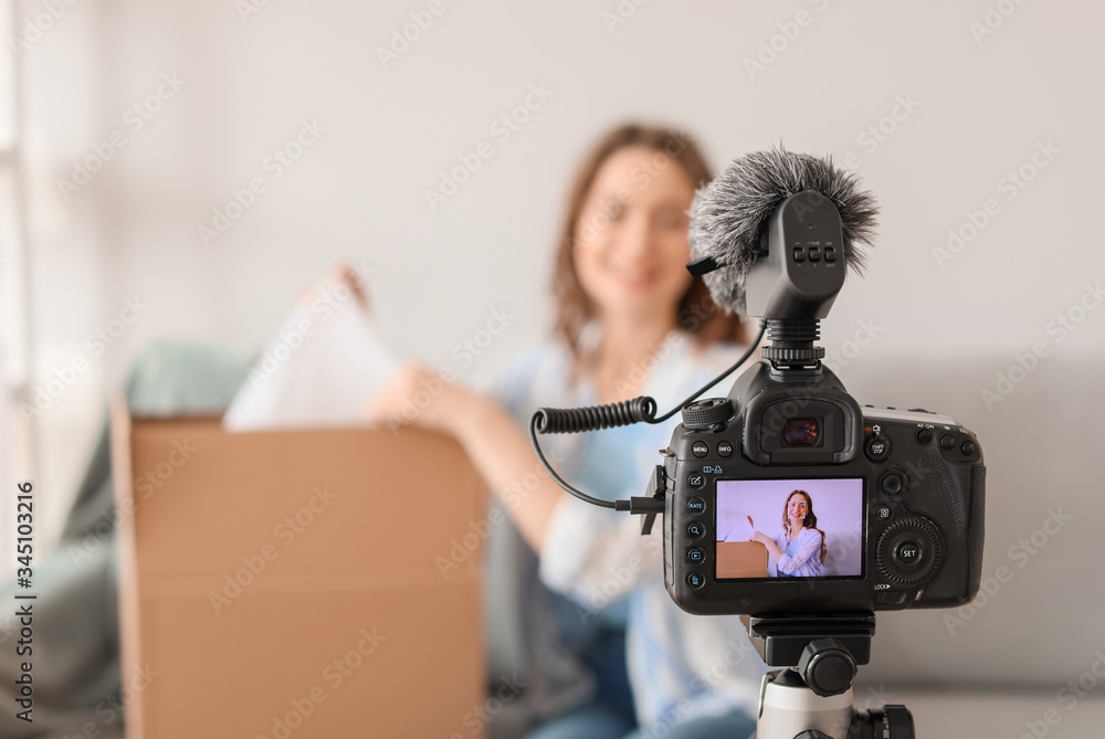 Young female blogger recording video while unpacking parcel at home