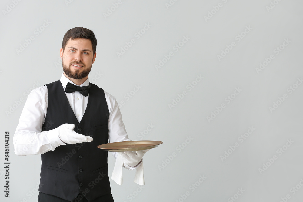 Male waiter with empty tray on grey background