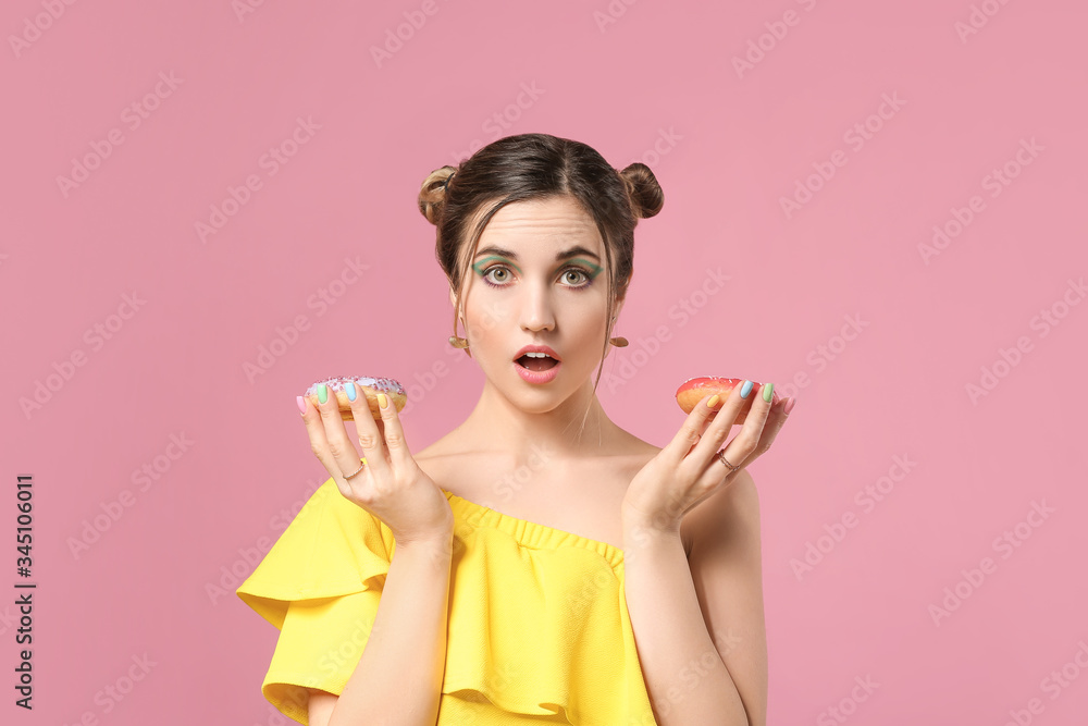 Surprised young woman with beautiful manicure and donuts on color background