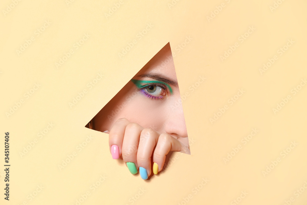 Young woman with beautiful manicure visible through cut color paper