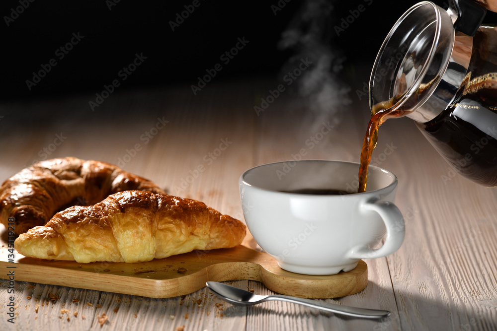 Pouring coffee with smoke on a cup and croissants on white wooden table